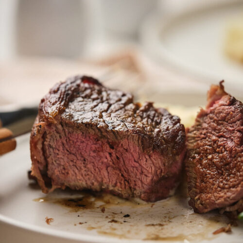 Bacon-wrapped beef tenderloin partially cut to reveal its pink interior.