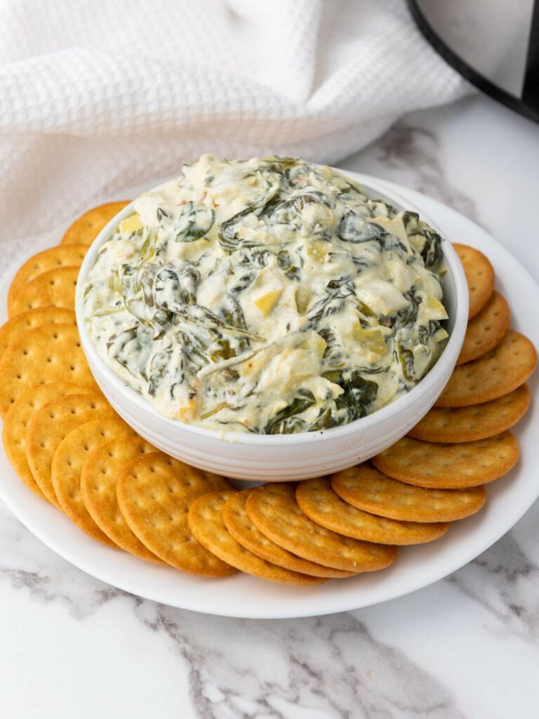 A bowl of spinach artichoke dip surrounded by round crackers.