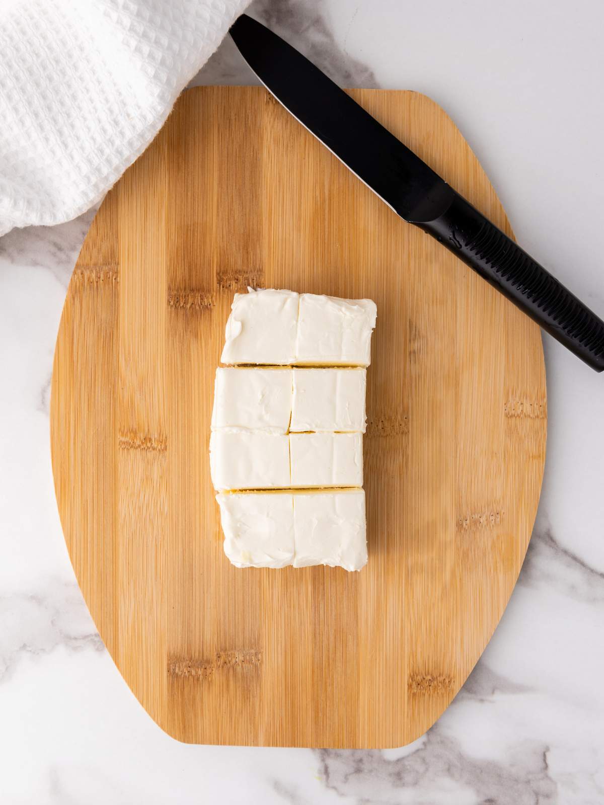 Sliced frosted cake on a wooden cutting board with a black knife and white cloth nearby.