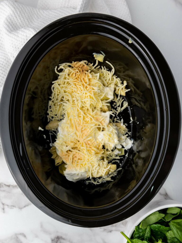 Ingredients including cheese in a slow cooker on a marble surface with a white towel nearby.