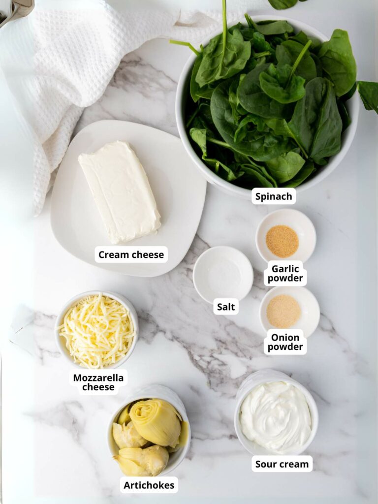 Ingredients for spinach artichoke dip on a marble surface.