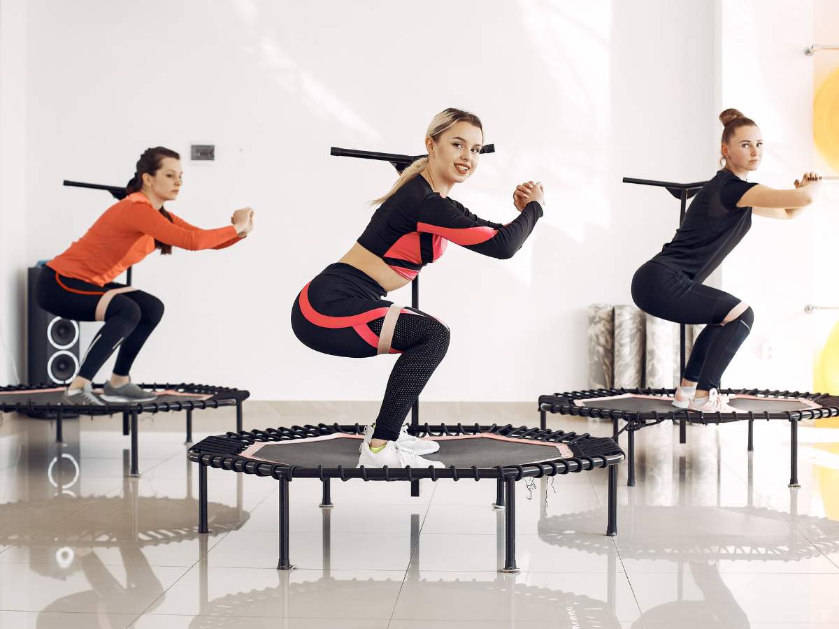 Three women exercise on mini trampolines in a bright room.