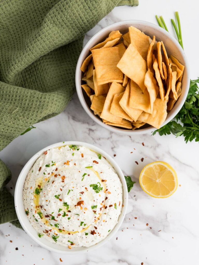 A bowl of feta dip garnished with herbs and spices .