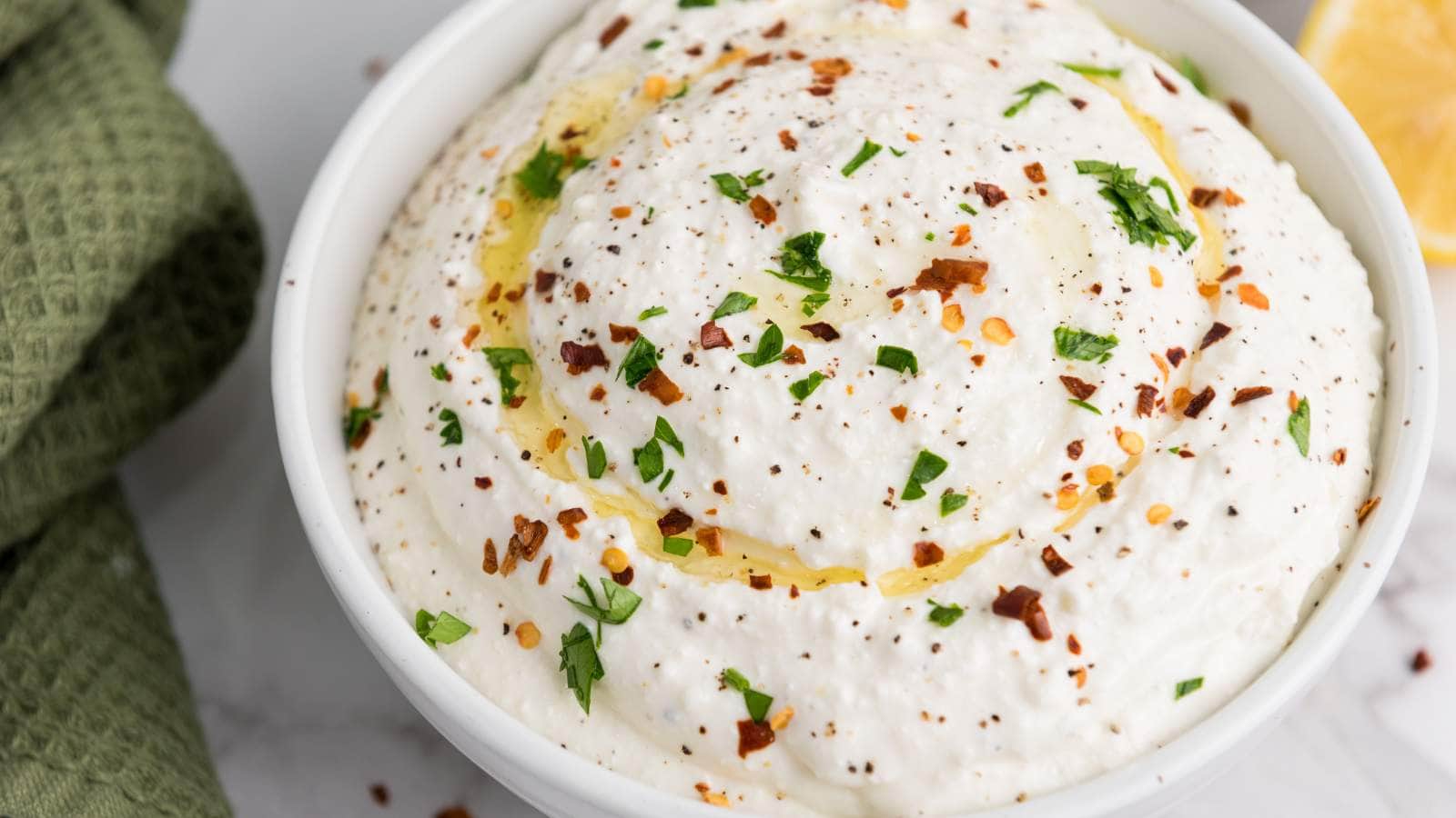 A bowl of feta dip garnished with olive oil, chopped parsley, and red pepper flakes.