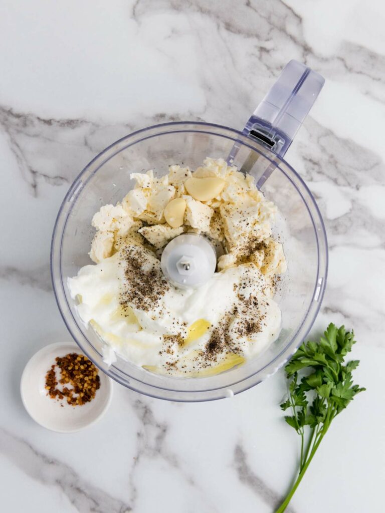 Food processor with cheese, garlic, yogurt, black pepper, and olive oil.