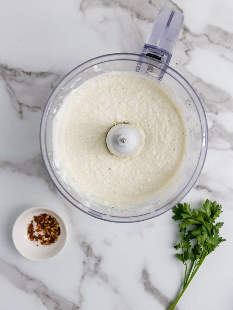 Food processor with creamy white mixture.