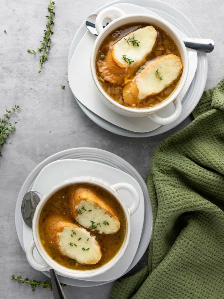 Two white bowls of French onion soup topped with toasted bread.