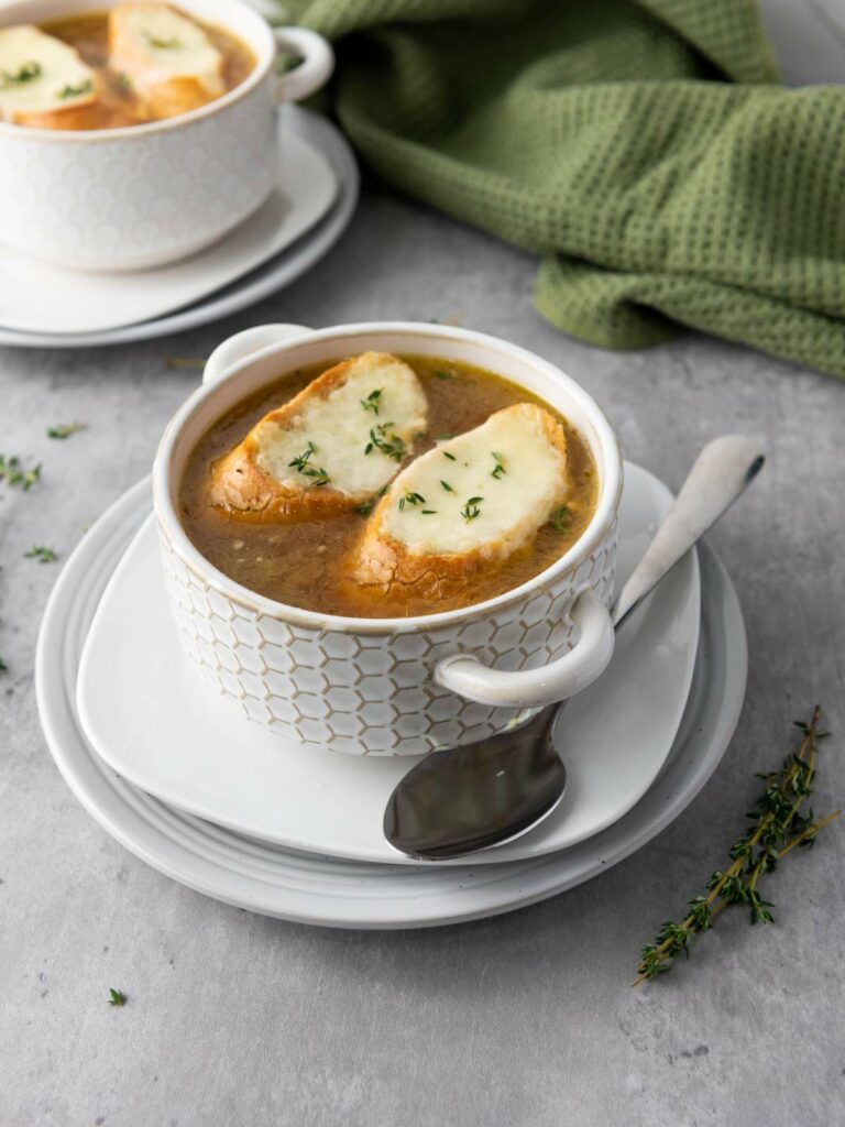 Two white bowls of French onion soup topped with toasted bread and melted cheese.