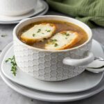 A bowl of soup topped with two slices of toasted bread and melted cheese.