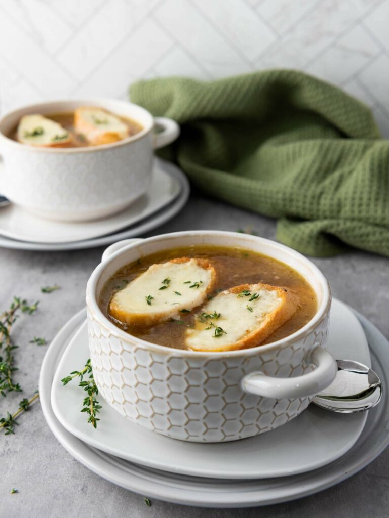 Two white bowls of soup topped with cheese-covered bread.