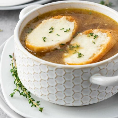 Bowl of onion soup with two slices of toasted bread topped with melted cheese and sprinkled with herbs.