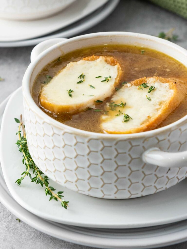 Bowl of onion soup with two slices of toasted bread topped with melted cheese and sprinkled with herbs.