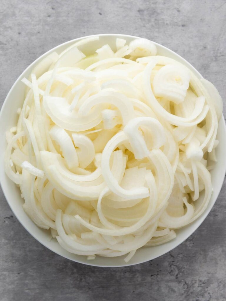 A white bowl filled with thinly sliced raw onions on a gray surface.