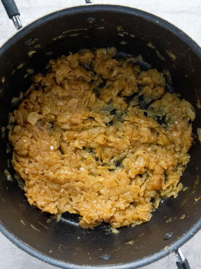 Caramelized onions in a black pot, evenly browned and softened, viewed from above.