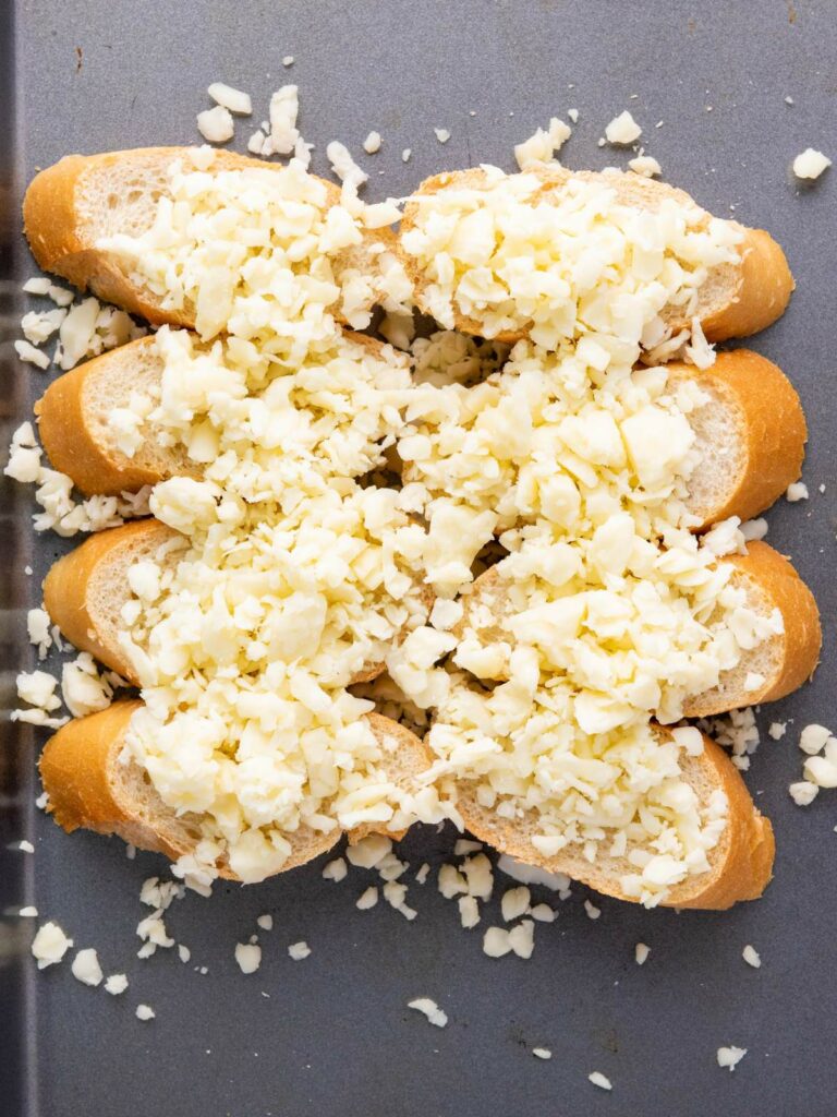 Slices of bread topped with shredded white cheese on a baking tray.