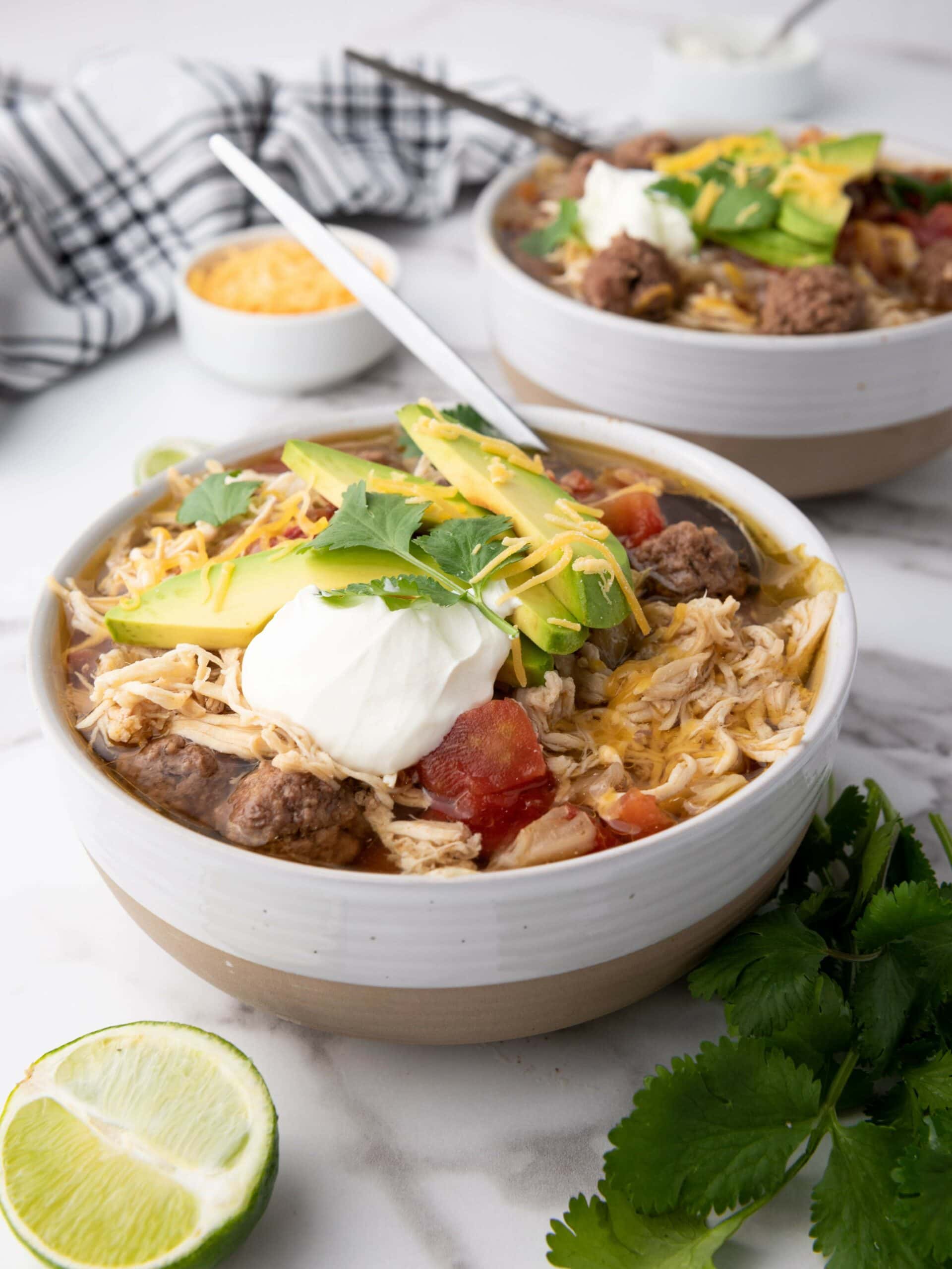 Two bowls oftaco soup on a marble surface, with a checkered cloth in the background.