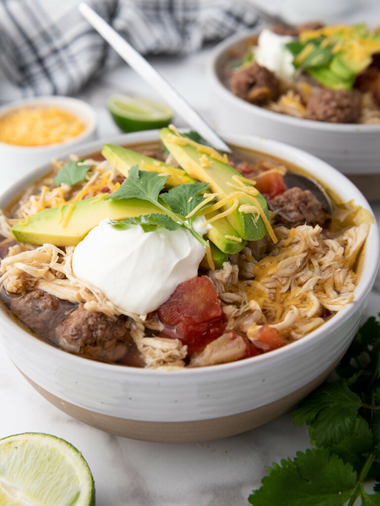 A bowl of soup with shredded chicken, avocado slices, sour cream, and cilantro on top.