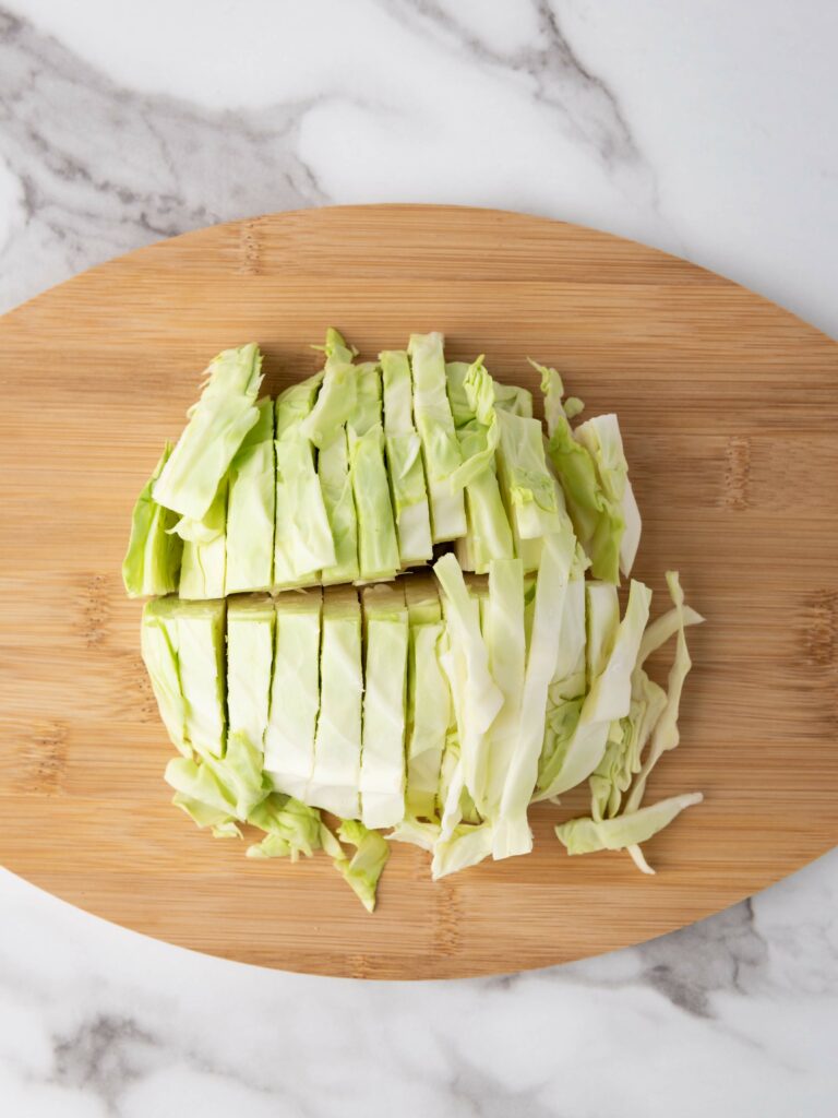 Chopped green cabbage on a wooden cutting board, placed on a marble surface.