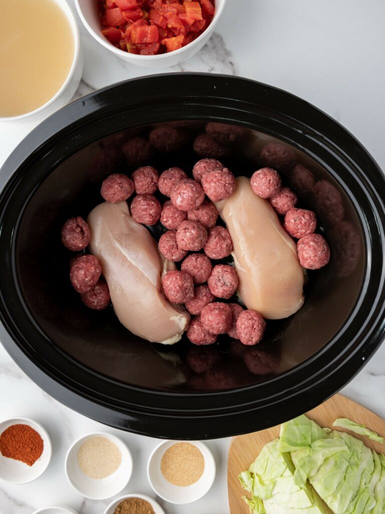 Slow cooker with raw chicken breasts, meatballs.