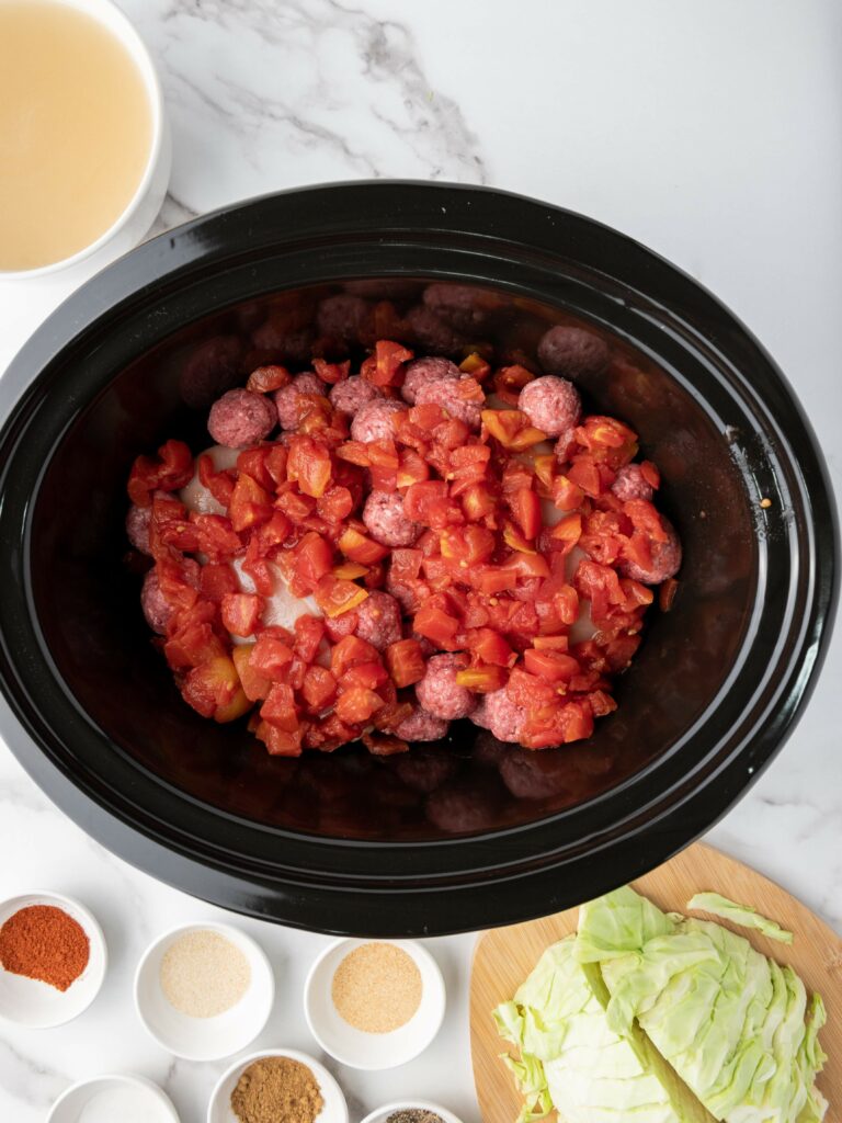 Slow cooker with diced tomatoes, meat, and onions.