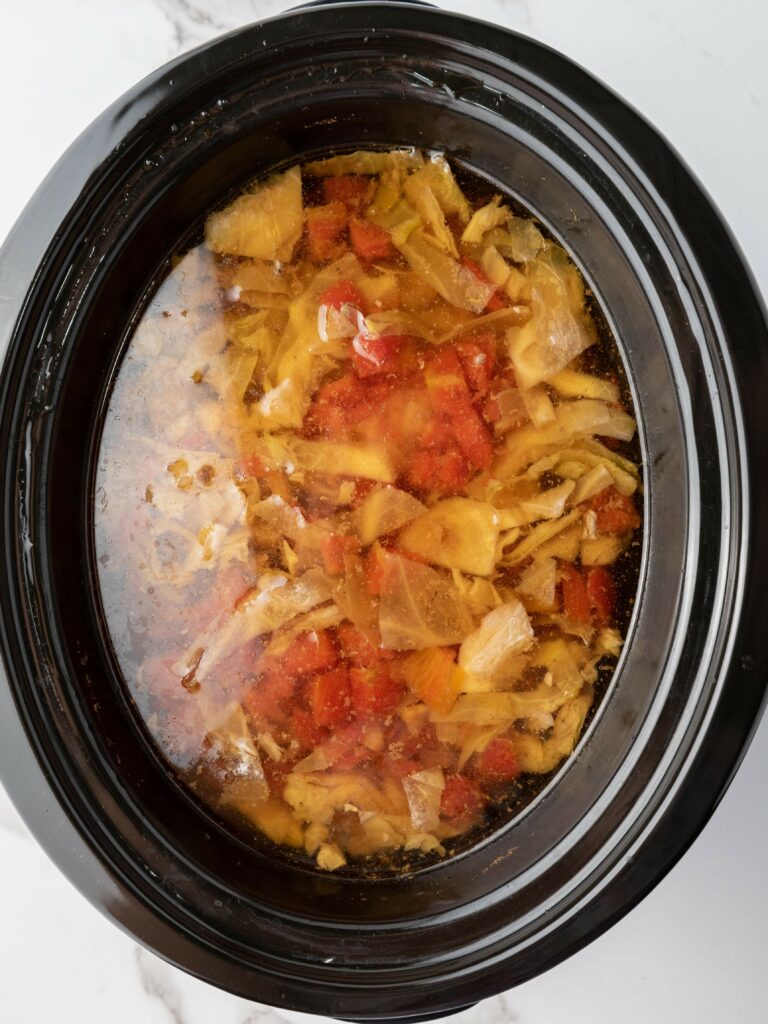 A slow cooker filled with cabbage soup, featuring visible chunks of cabbage, tomatoes, and other vegetables in broth.