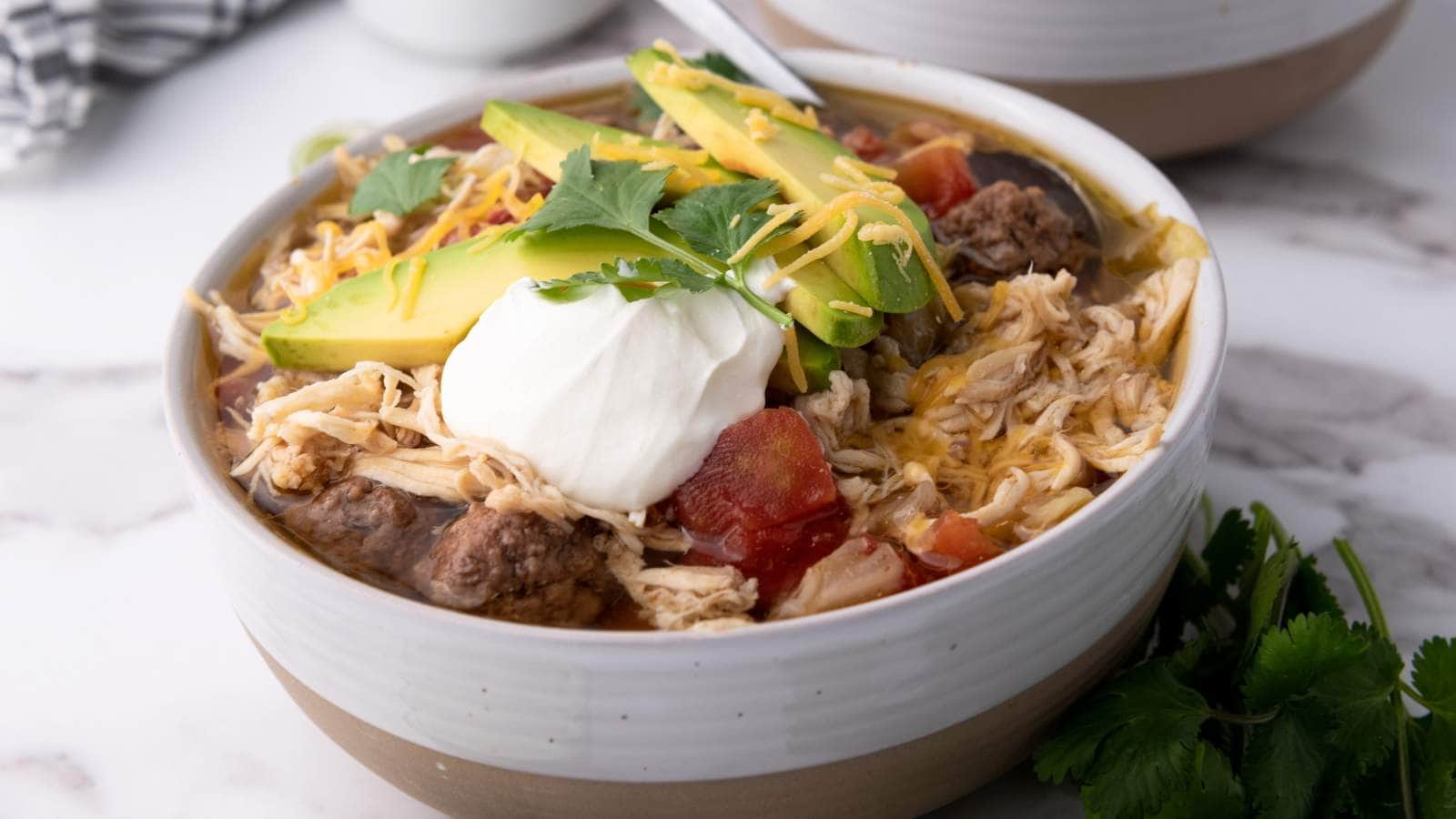 A bowl oftaco soup topped with avocado slices, sour cream, shredded cheese, and cilantro.