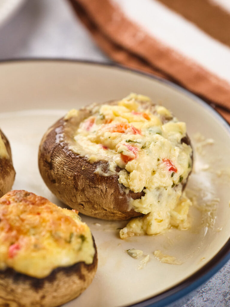 Stuffed mushroom caps filled with a creamy mixture, served on a beige plate.