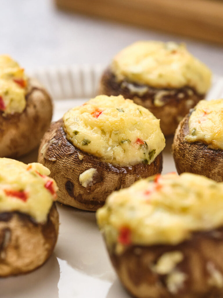 Stuffed mushrooms on a white plate, filled with a cheese and herb mixture.