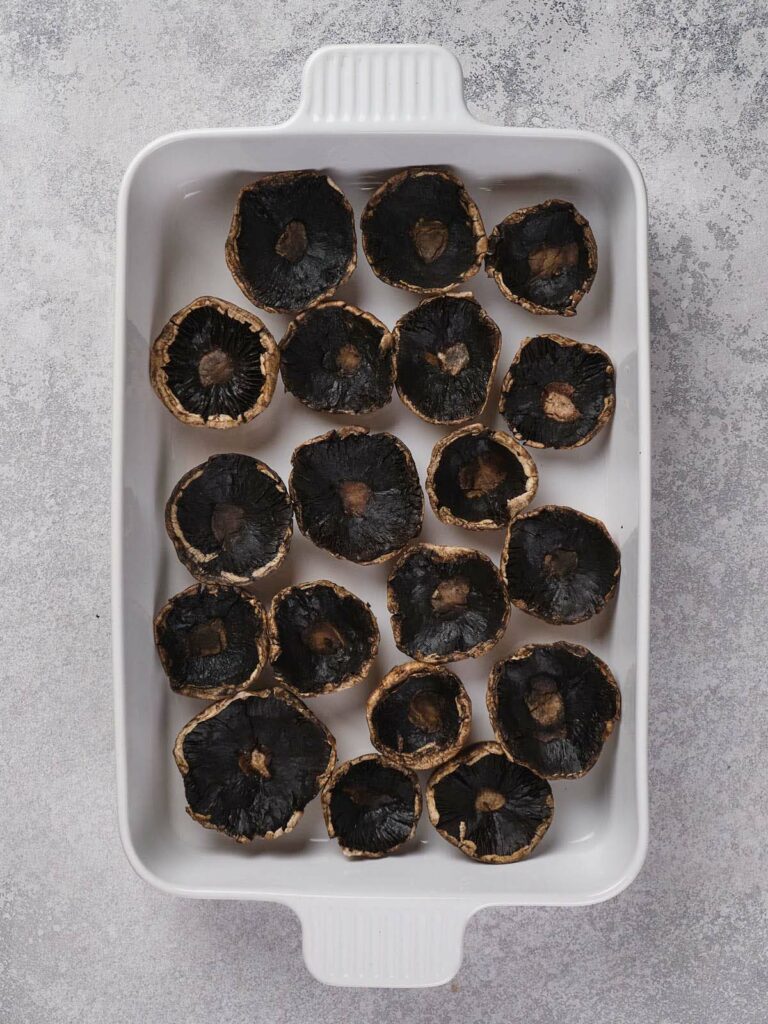 White baking dish containing upturned mushroom caps placed evenly in rows on a gray textured surface.