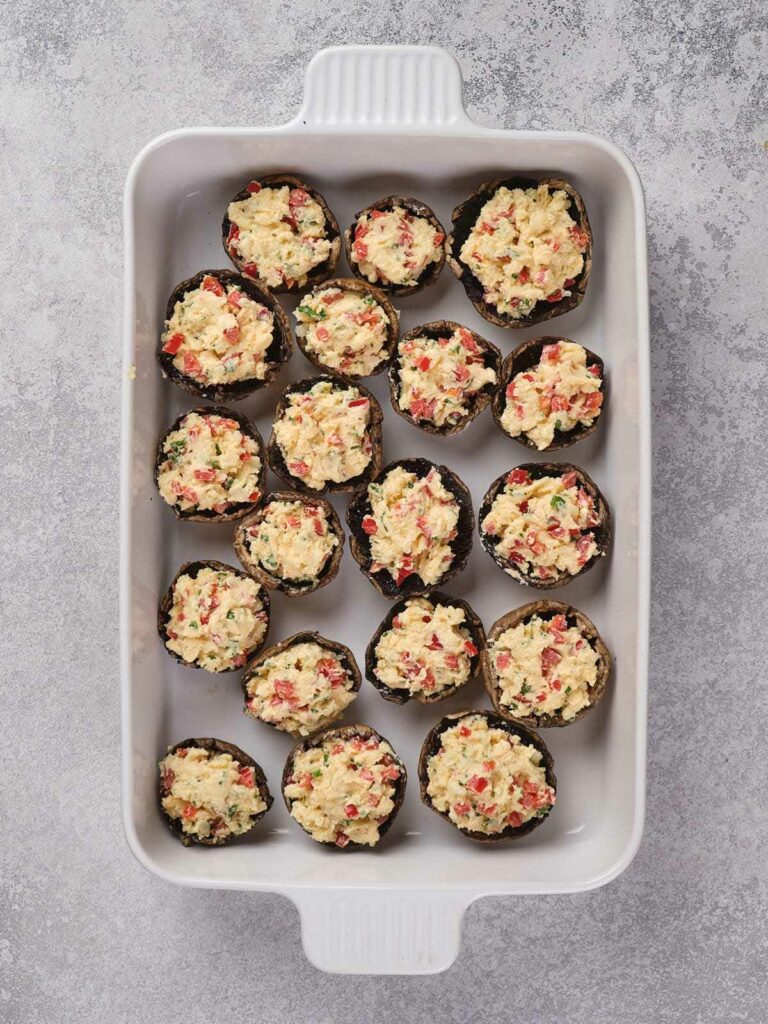 A white baking dish filled with multiple stuffed mushrooms arranged in rows.