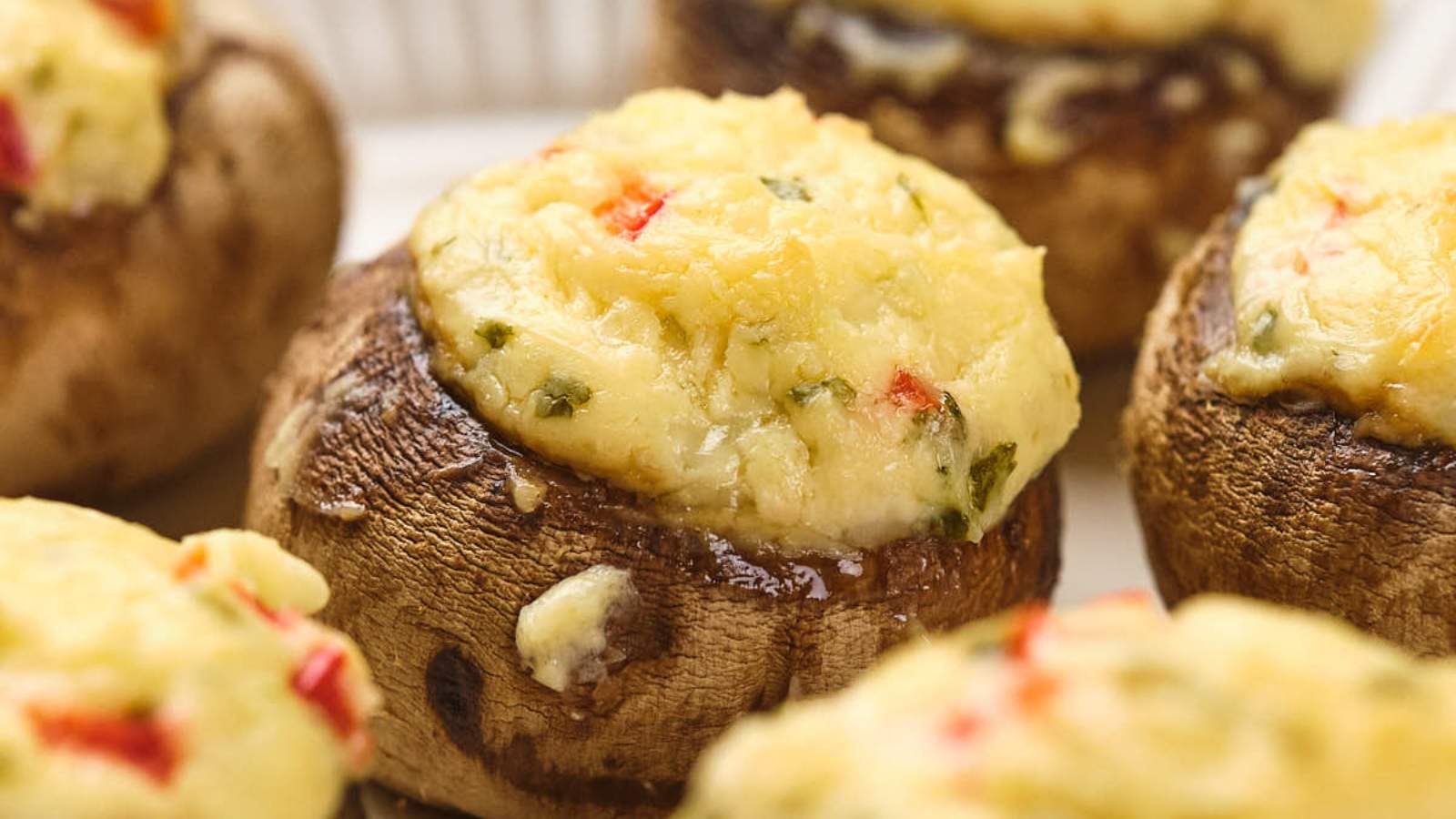 Stuffed mushrooms topped with cream cheese, garnished with herbs and red pepper bits.