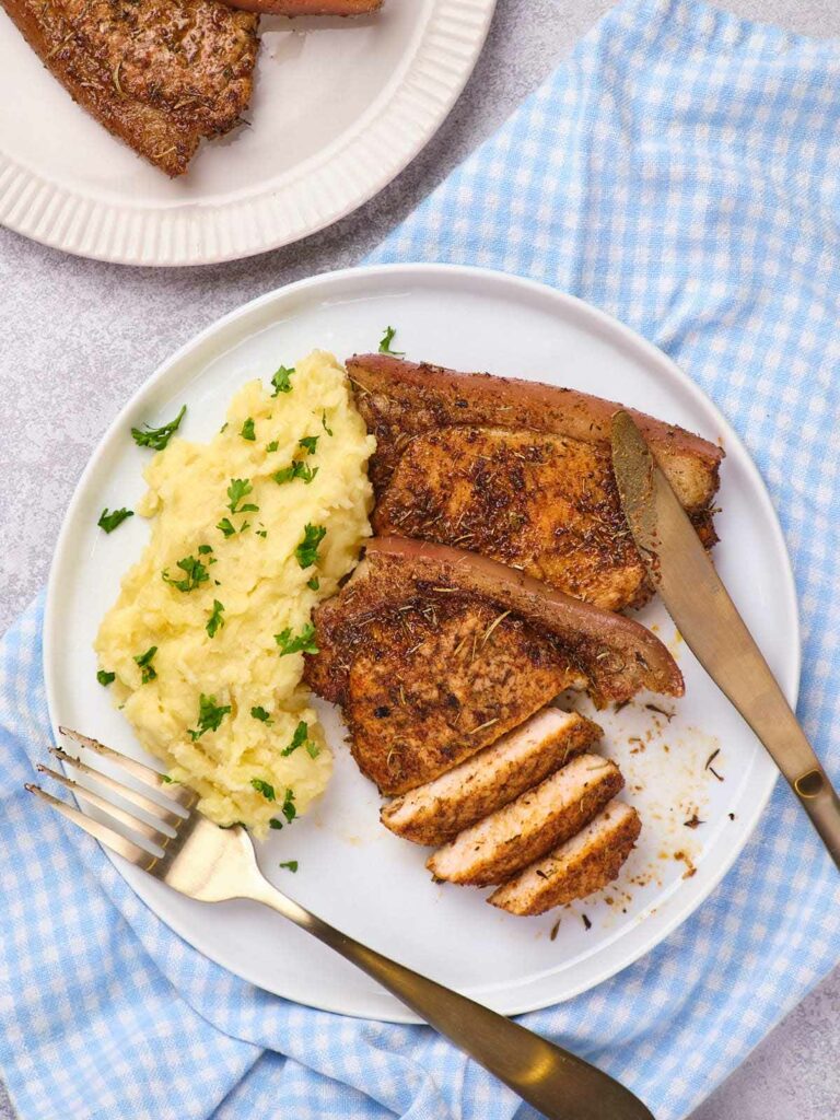 A white plate with sliced seasoned boneless pork chops and mashed potatoes.