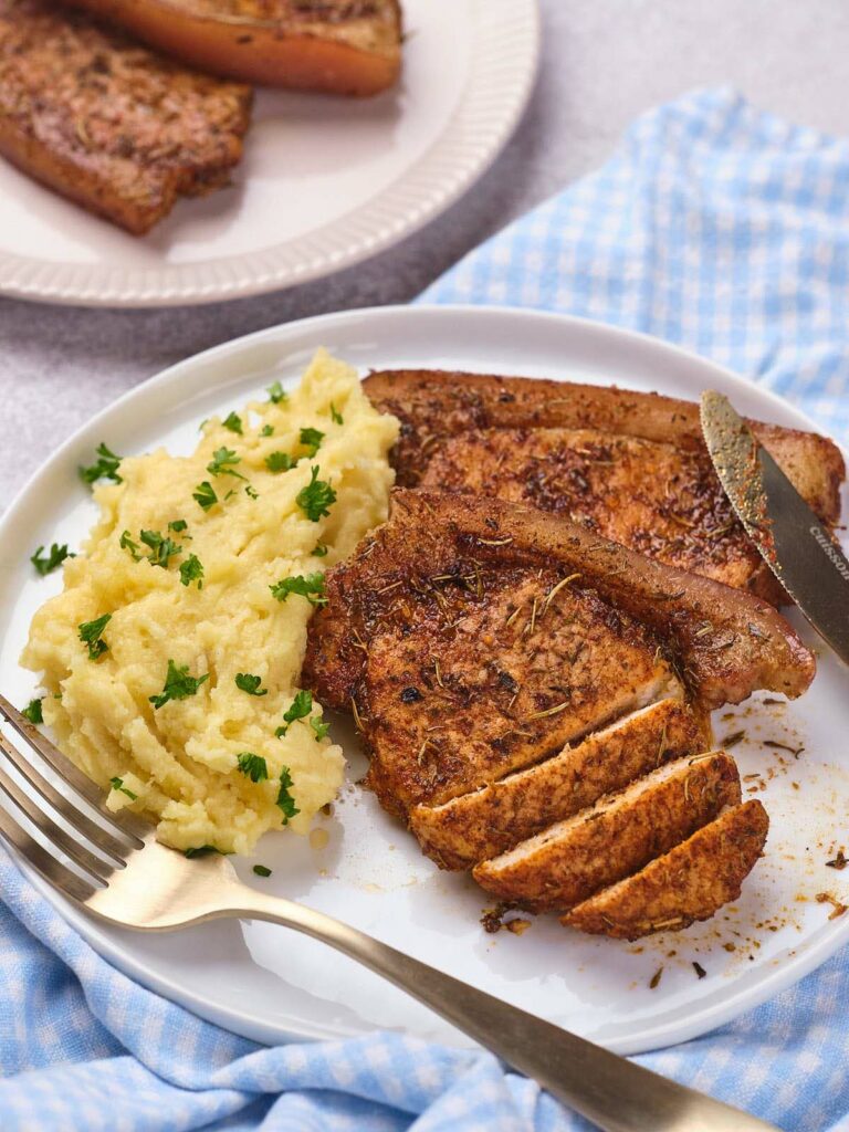 Plate of air fryer boneless pork chops with mashed potatoes topped with parsley.