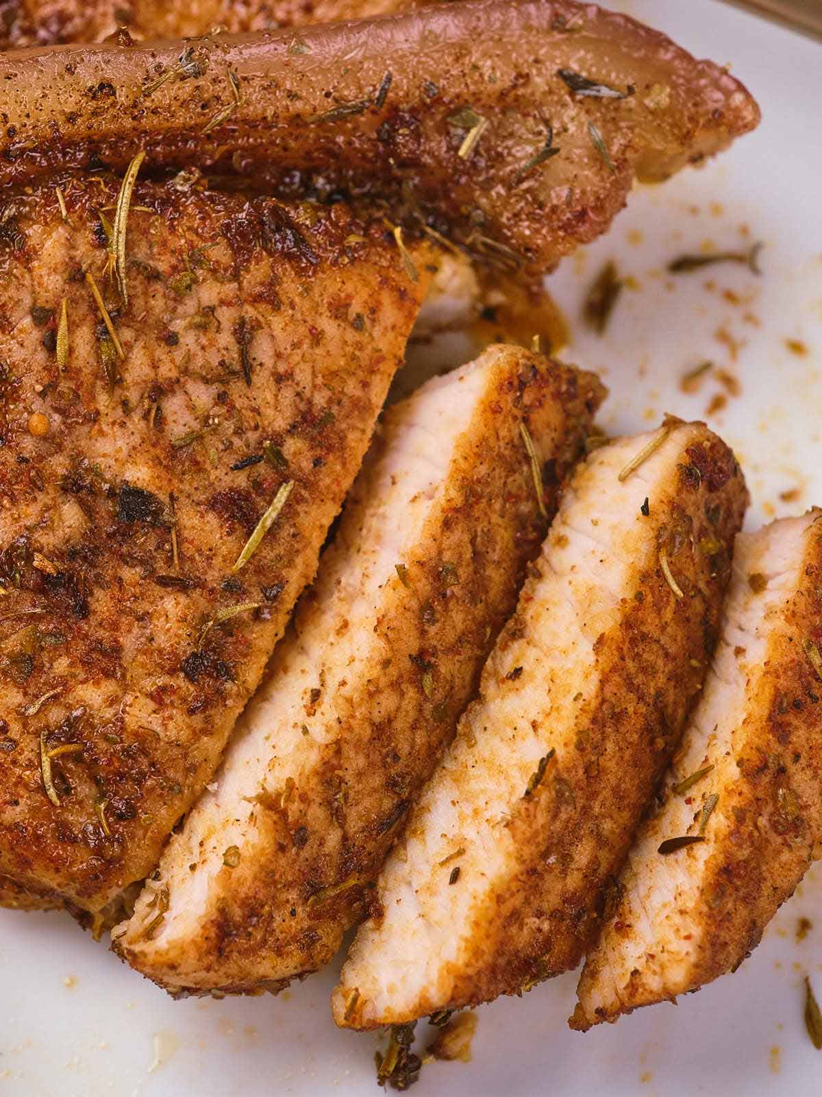 Sliced seasoned boneless pork chops with herbs on a plate.