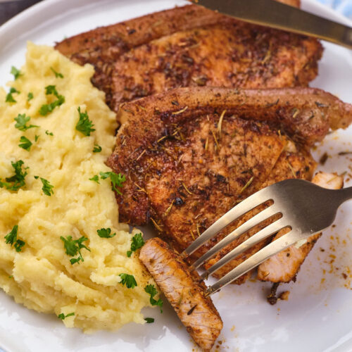 Plate of air fryer boneless pork chops with a serving of mashed potatoes, garnished with chopped parsley.