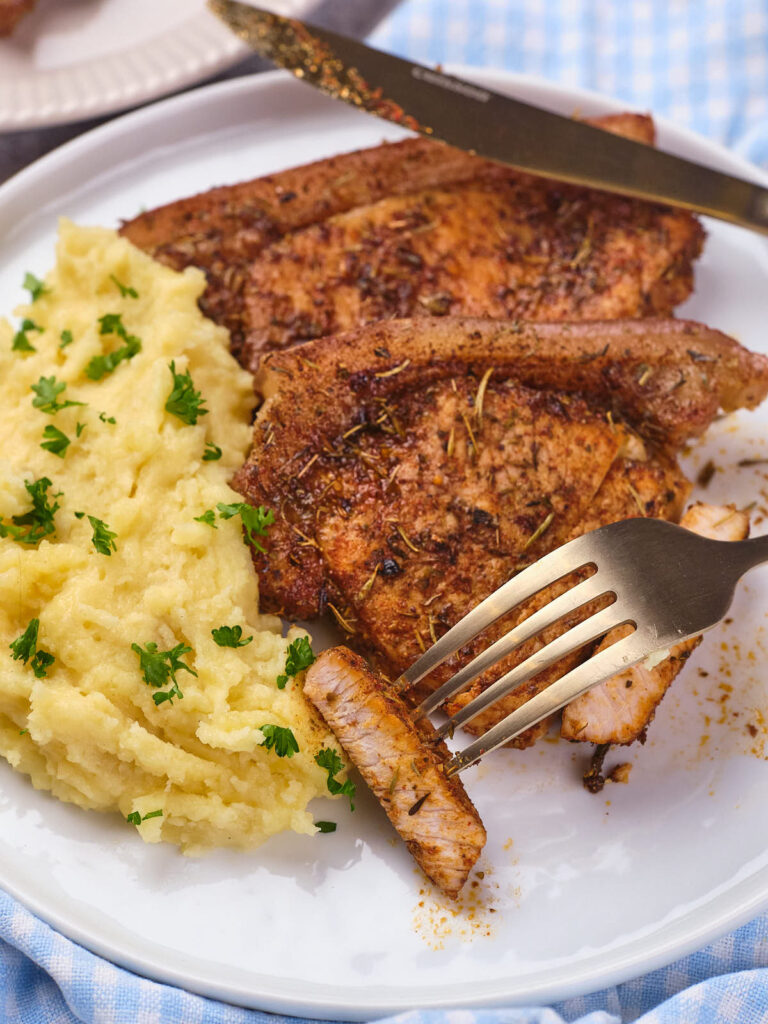 Plate of air fryer boneless pork chops with a serving of mashed potatoes, garnished with chopped parsley.