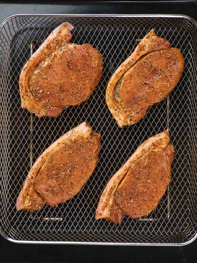 Four seasoned pork chops on a grill rack, seen from above.