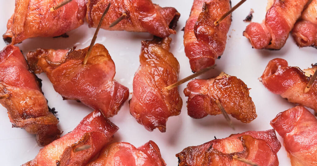 pineapple and bacon bites secured with toothpicks arranged on a white surface.