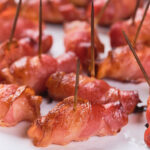 Bacon-wrapped appetizers secured with toothpicks are arranged on a white plate.