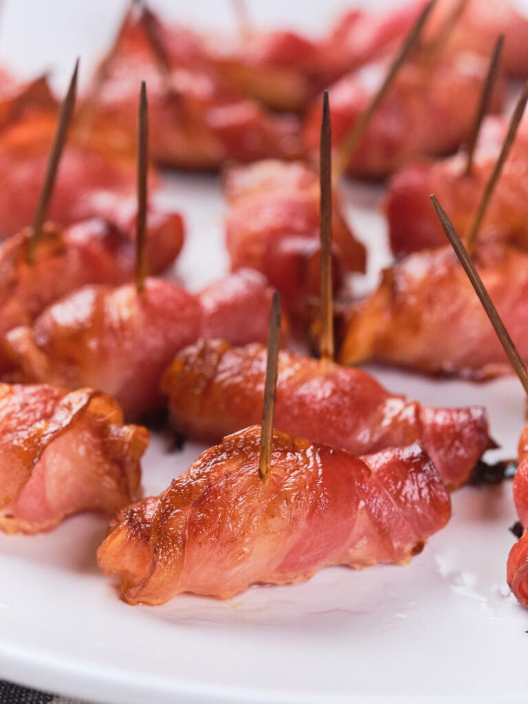 Bacon-wrapped appetizers secured with toothpicks are arranged on a white plate.