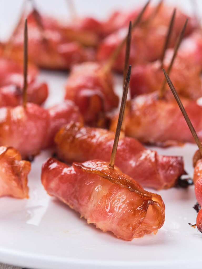 Bacon-wrapped appetizers on a white plate, each secured with a toothpick.