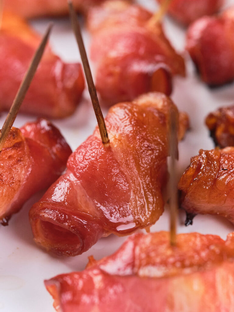 Bacon-wrapped sausages with toothpicks on a white plate.