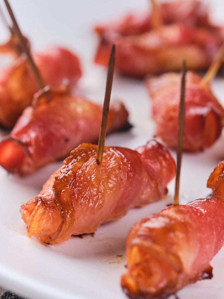 Bacon-wrapped sausages secured with toothpicks on a white plate.