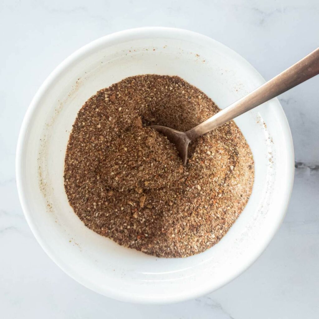 Bowl of mixed spices with a spoon on a white marble surface.