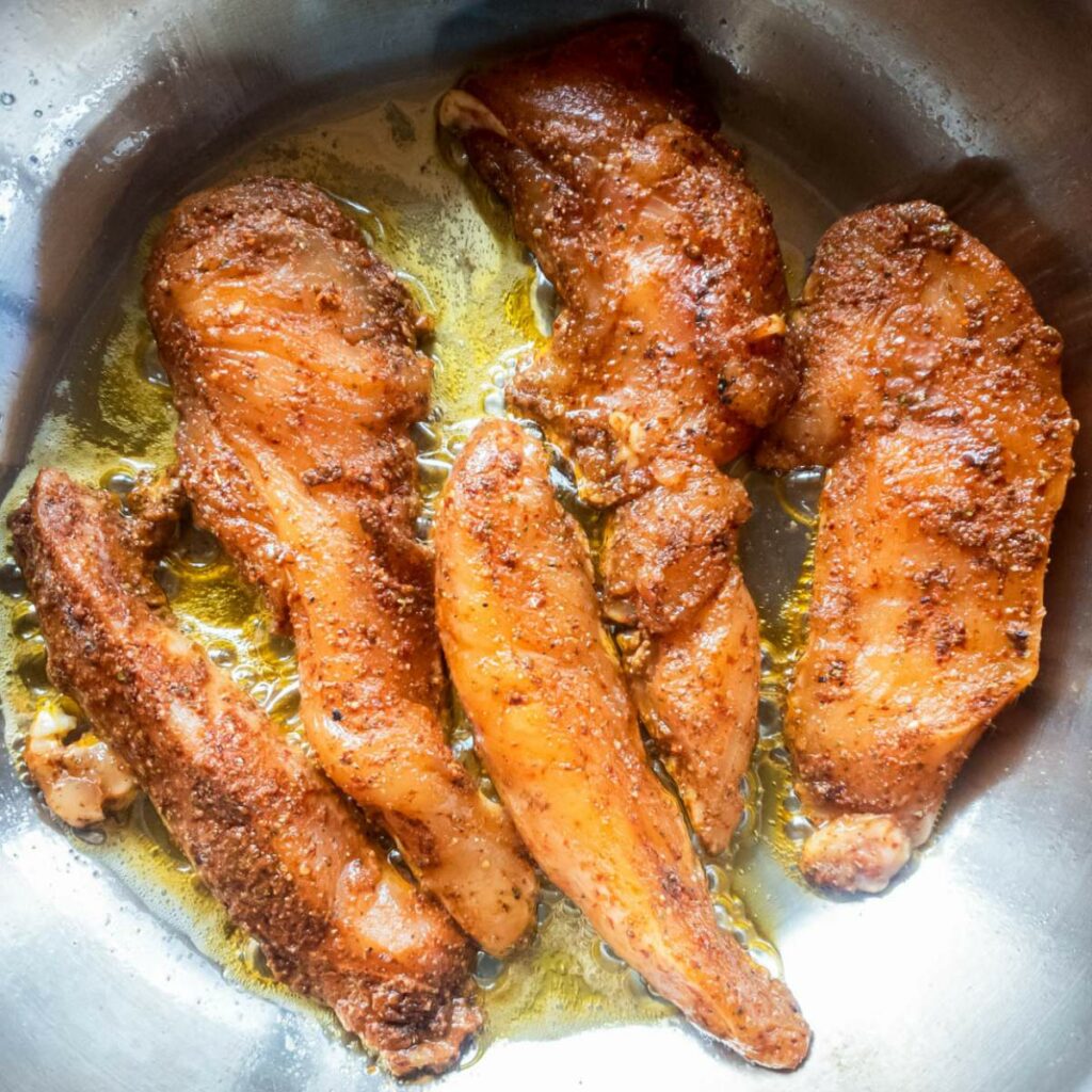 Six seasoned chicken tenders cooking in a pan with oil.