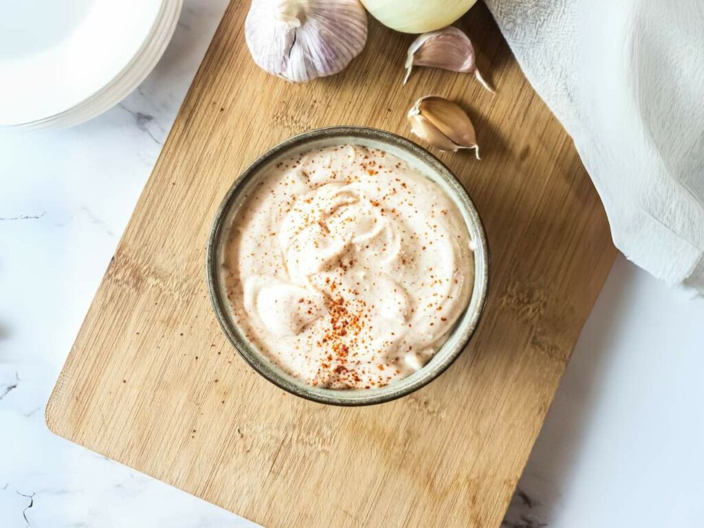 A bowl of chipotle mayonnaise sprinkled with paprika on a wooden board.