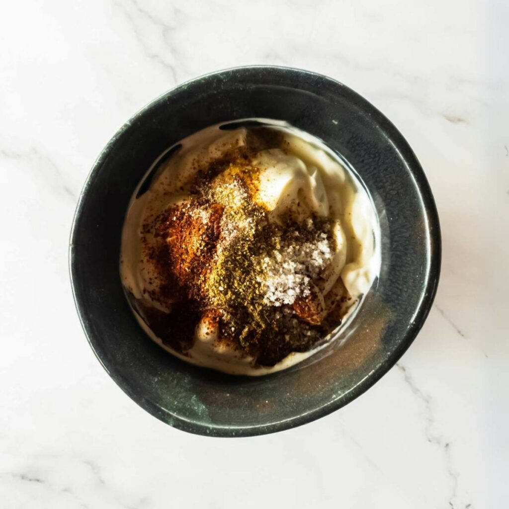 A black bowl containing yogurt topped with various spices sits on a white marble surface.