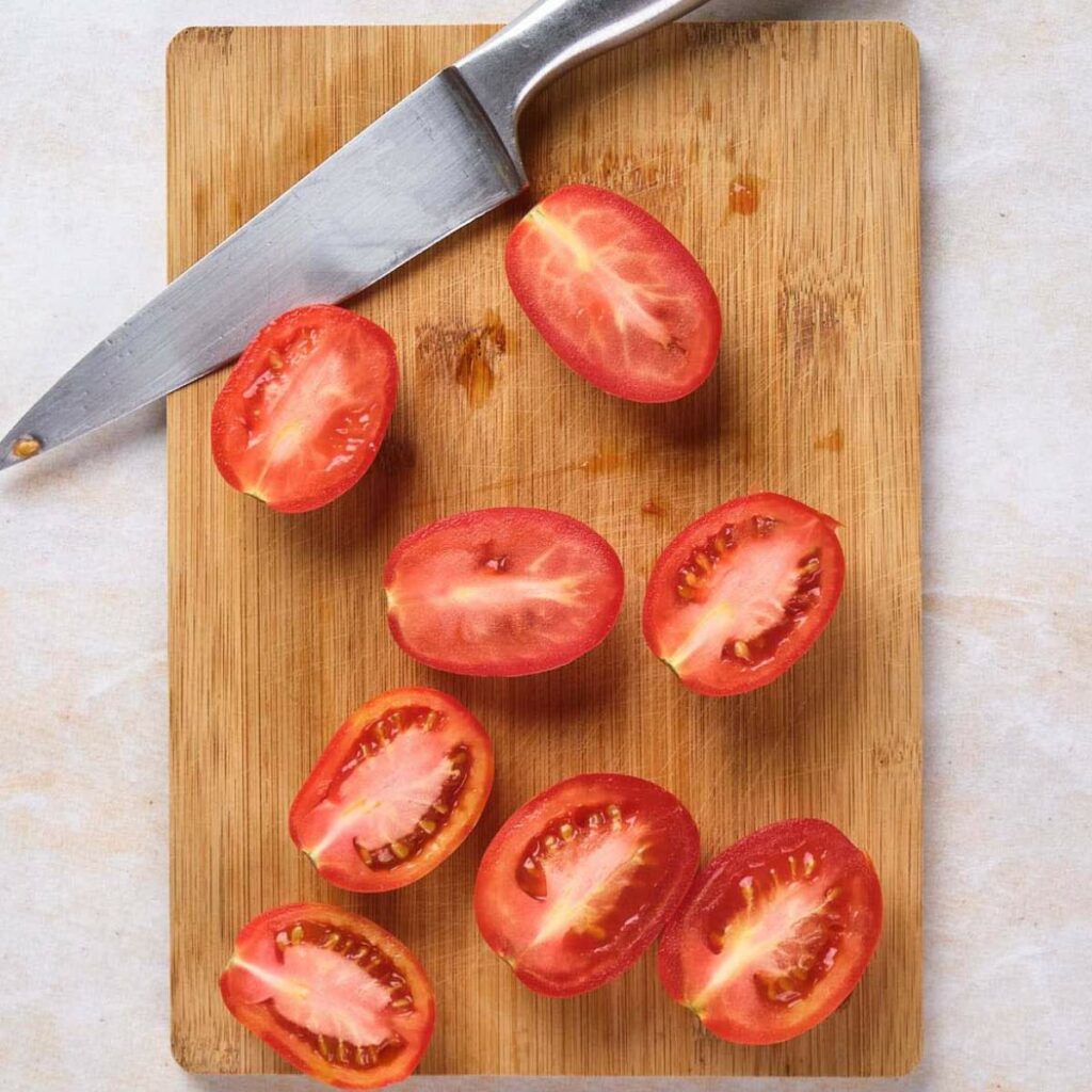 Tomato halves and a knife on a wooden cutting board.