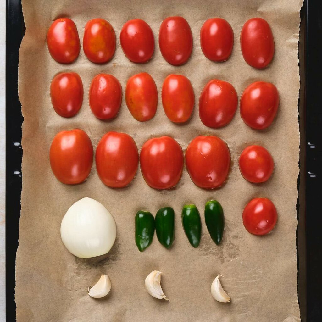 Tomatoes, an onion, jalapeños, and garlic cloves arranged on parchment paper.