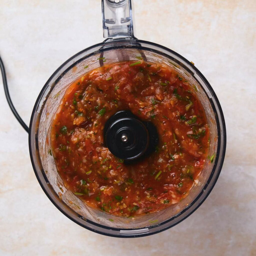 Top view of a food processor containing blended salsa with visible red and green ingredients.